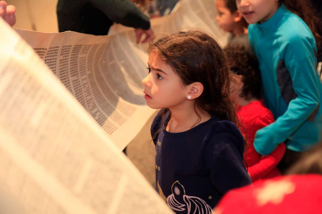 Temple Israel & JCC Girl looking at unwrapped Torah during Simchat Torah activity with our NNJJA religious school